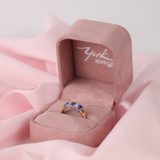 Pink jewellery box with a diamond & Sapphire ring featuring blue gemstones on a pink fabric background
