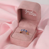 Gold ring with blue sapphires and diamonds in a pink jewellery box labelled 'York Jewellers' on a pink fabric background.