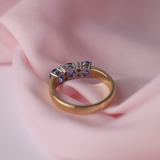 Yellow and white gold ring with blue sapphires and diamonds on a pink fabric background.