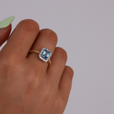 Close-up of 9ct yellow gold ring showcasing an emerald cut blue topaz with a diamond halo, available at York Jewellers Penrith.