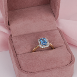 9ct yellow gold halo ring featuring a claw set emerald cut blue topaz (7 x 5mm) surrounded by 20 carcelated set round brilliant cut diamonds (0.17ct total, H-I colour, P1 clarity), available at York Jewellers Penrith and Warriewood (Sydney).