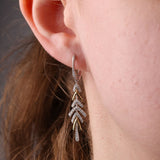 Close-up of 18ct yellow and white gold earrings showcasing carcelated round brilliant cut diamonds (0.56ct total, H/SI) set within arrow-like drop details available at York Jewellers Penrith.