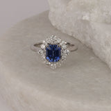 Detail shot of round brilliant cut diamond halo (0.72ct total, H/SI) surrounding a natural blue sapphire on an 18ct white gold dress ring.