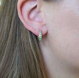 9ct yellow gold emerald and diamond huggie hoop earrings worn on the ear showing colour and sparkle.