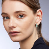 9ct white gold Jules Huggie Earrings worn on the ear showing princess cut teal sapphires and shifting colour.