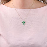 18ct yellow gold emerald cross pendant worn at the collarbone showing rich green gemstones and diamond accent.