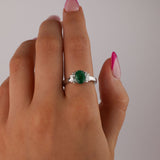  18ct white gold emerald ring worn on hand showing rich green oval gemstone and tapered diamond detailing.