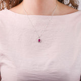 18ct white gold ruby halo pendant worn at the collarbone showing rich red oval gemstone and sparkling diamond frame.