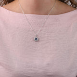 18ct white gold sapphire halo pendant worn at the collarbone showing rich blue square gemstone and sparkling diamond frame.