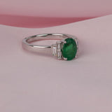 Detail shot of end set tapered baguette diamonds (0.14ct total, H/SI) flanking a natural oval emerald on an 18ct white gold ring.